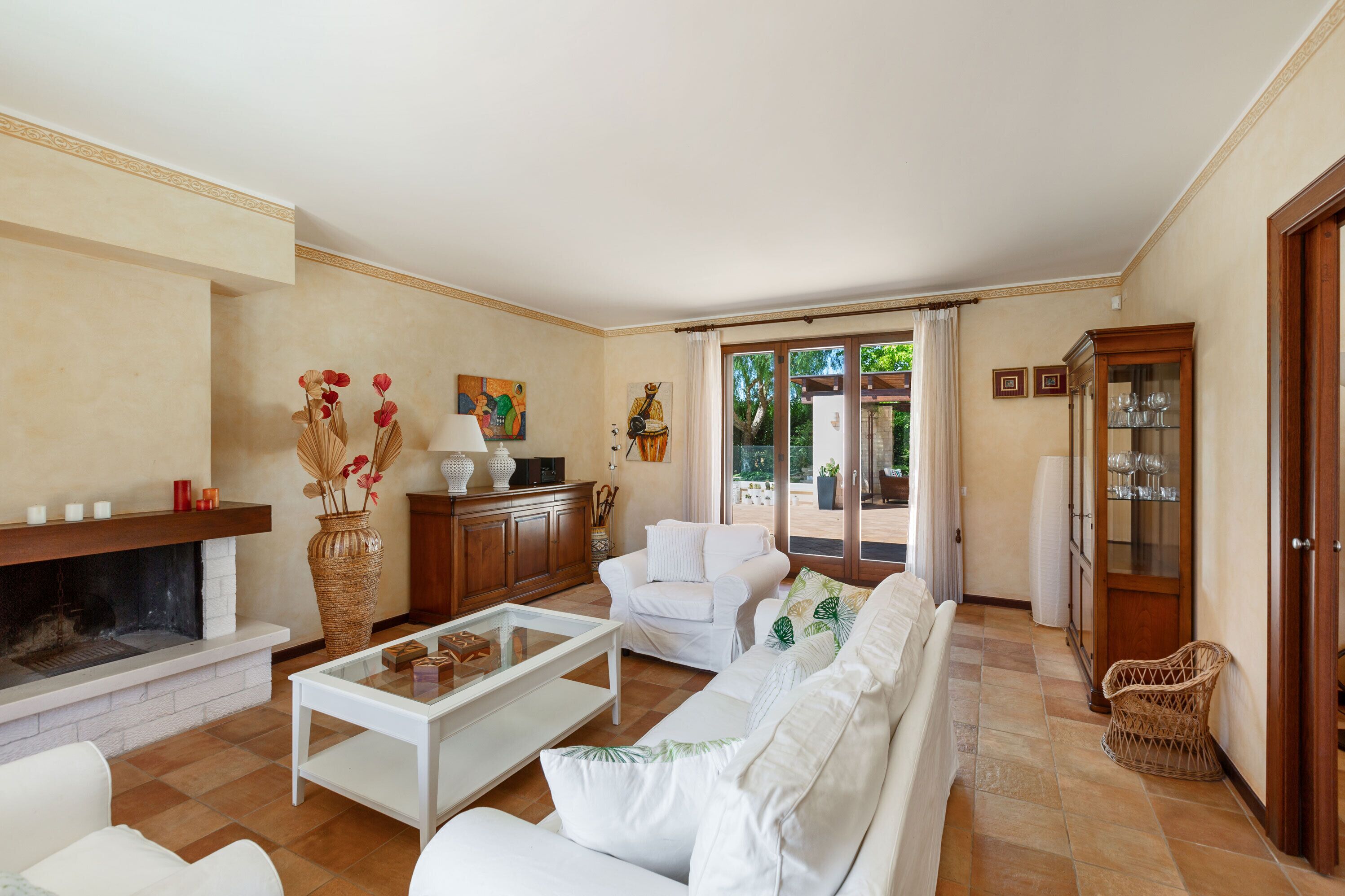 A living room with a fireplace, white sofas, a coffee table, and a dining area with a cabinet.