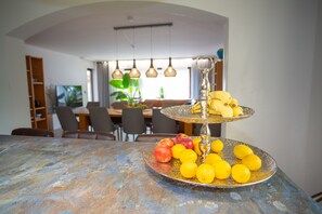 A dining area with a table set for two, featuring a fruit platter and a vase.
