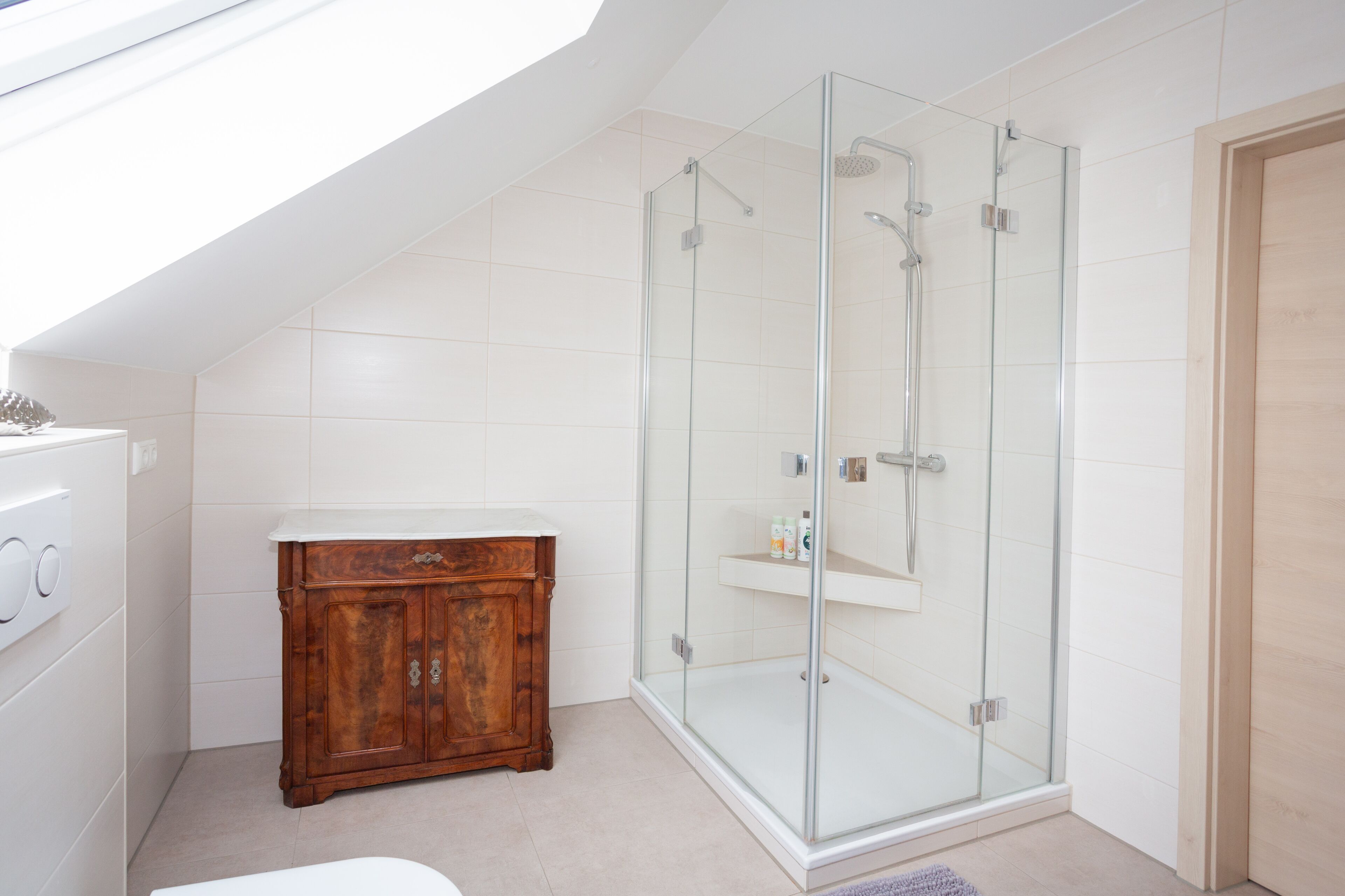 A modern bathroom with a glass-enclosed shower, a wooden vanity, and a white tiled floor.