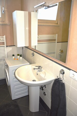 A bathroom with a sink, mirror, towel rack, and a washing machine. - Appartamento la Perla (Puegnago del Garda)