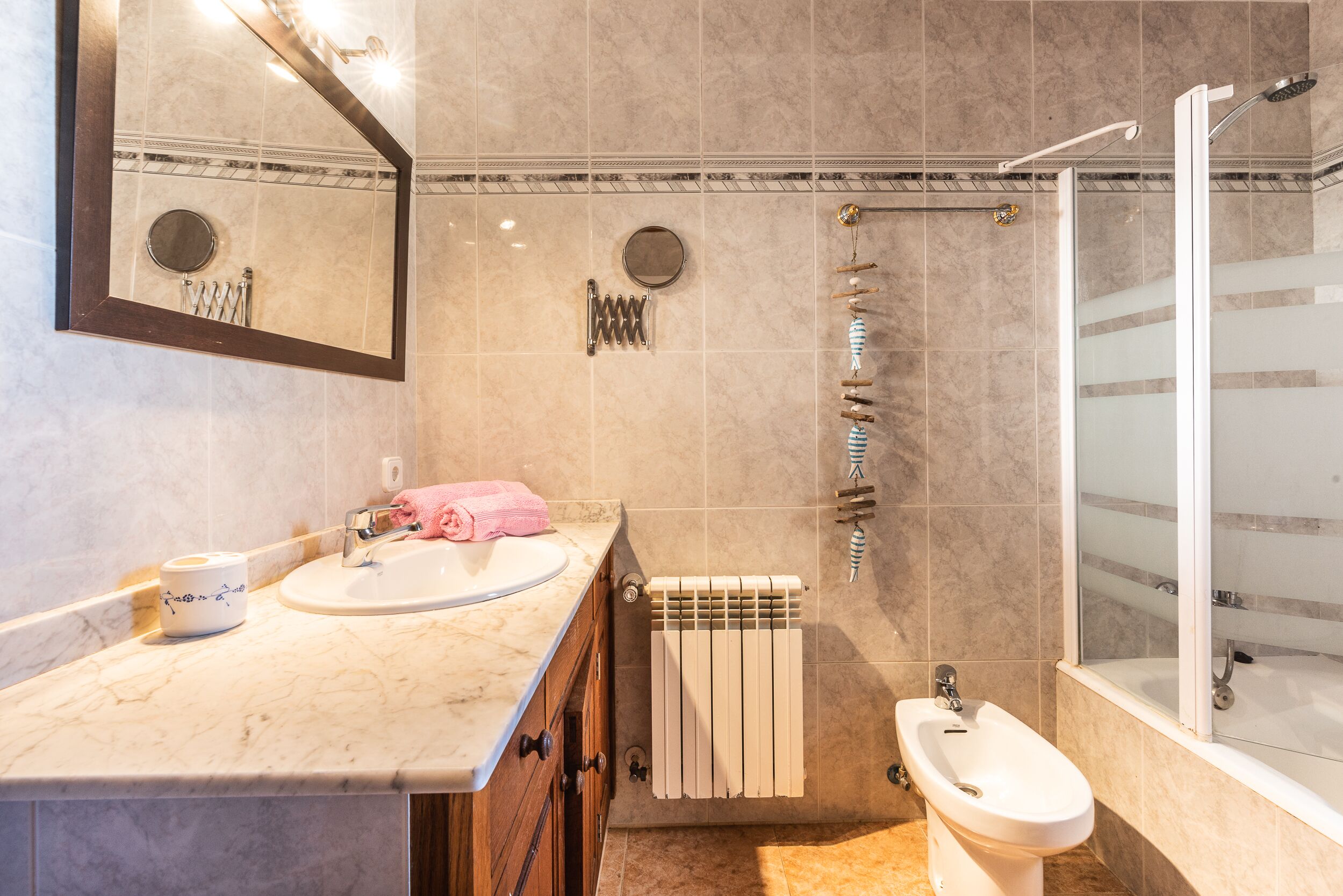 Et badeværelse med vask i marmor, et spejl, et toilet, et bidet og en brusekabine med glasvægge.