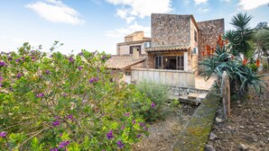 Eine mediterran gestaltete Villa mit Steinmauern, einem Ziegeldach und einem Garten mit violetten Blumen.