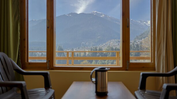 A room with a table and two chairs, a window with a view of a mountain. - Private Room in Manali, Mountain and River view Near Manali-4 (Bashisht)