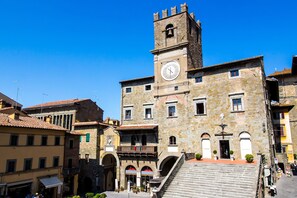A historic stone building with a clock tower, arched doorways, and a staircase leading to an upper level. - Fratta Apartments (Cortona)