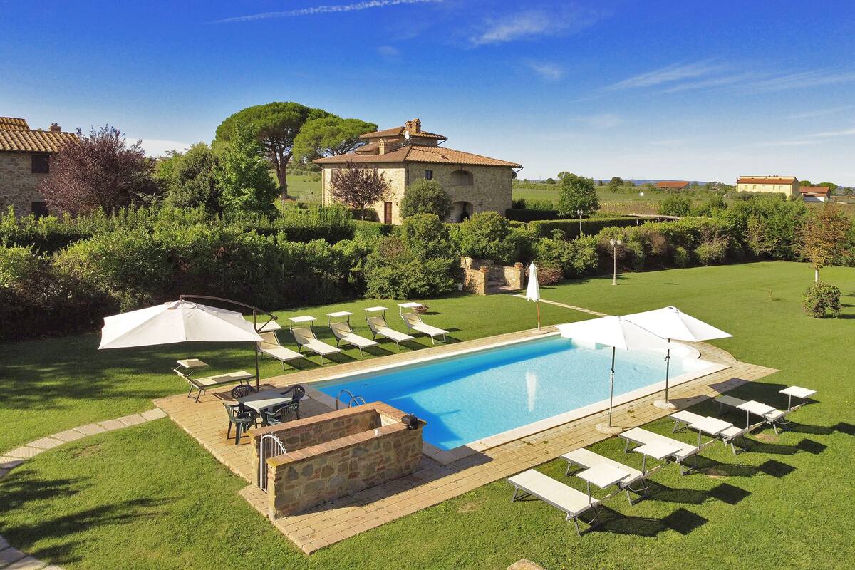 A swimming pool with lounge chairs and umbrellas, surrounded by a well-maintained lawn and stone buildings.