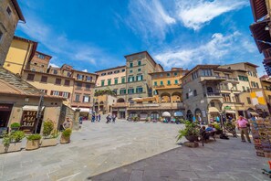 A historic square with stone buildings, outdoor seating, and a clear blue sky. - Fratta Apartments (Cortona)