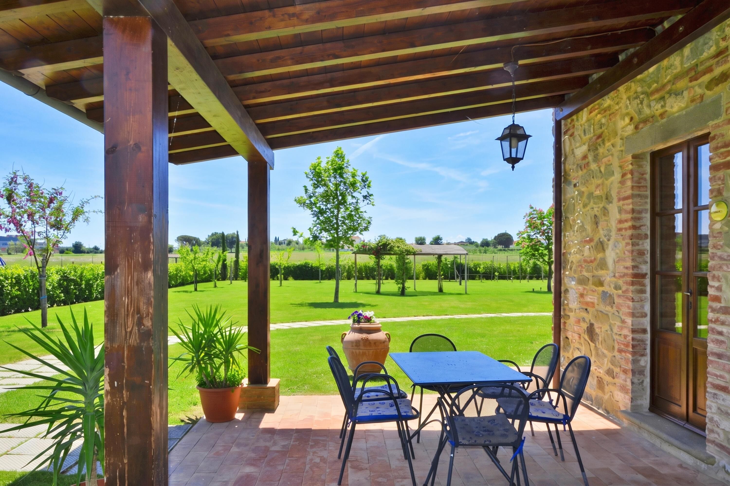 A covered patio with a table and chairs, a potted plant, and a view of a vineyard.