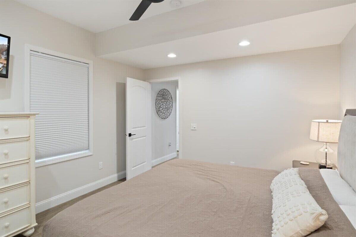 Un dormitorio con cama, cómoda, puerta y una obra de arte colgada en la pared.