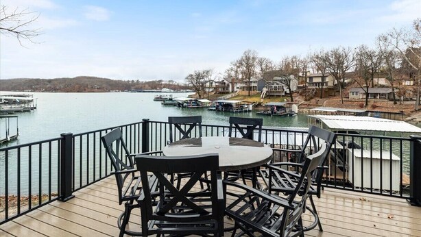 Eine Terrasse mit Tisch und Stühlen mit Blick auf einen See, im Hintergrund Boote und Häuser.