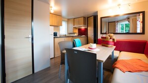 A compact kitchenette with a microwave, stove, and cabinets. There is a dining table with chairs and a red sofa. A teddy bear is placed on the sofa. - Cottage Family (Crêches-sur-Saône)