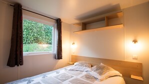 A bedroom with a bed, a window with curtains, and built-in shelves. - Cottage Family (Crêches-sur-Saône)