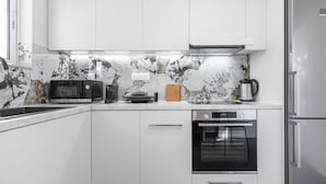 Eine moderne Küche mit weißen Schränken, einer Marmor-Spritzschutzleiste, einer Mikrowelle, einer Kaffeemaschine und einem Backofen.