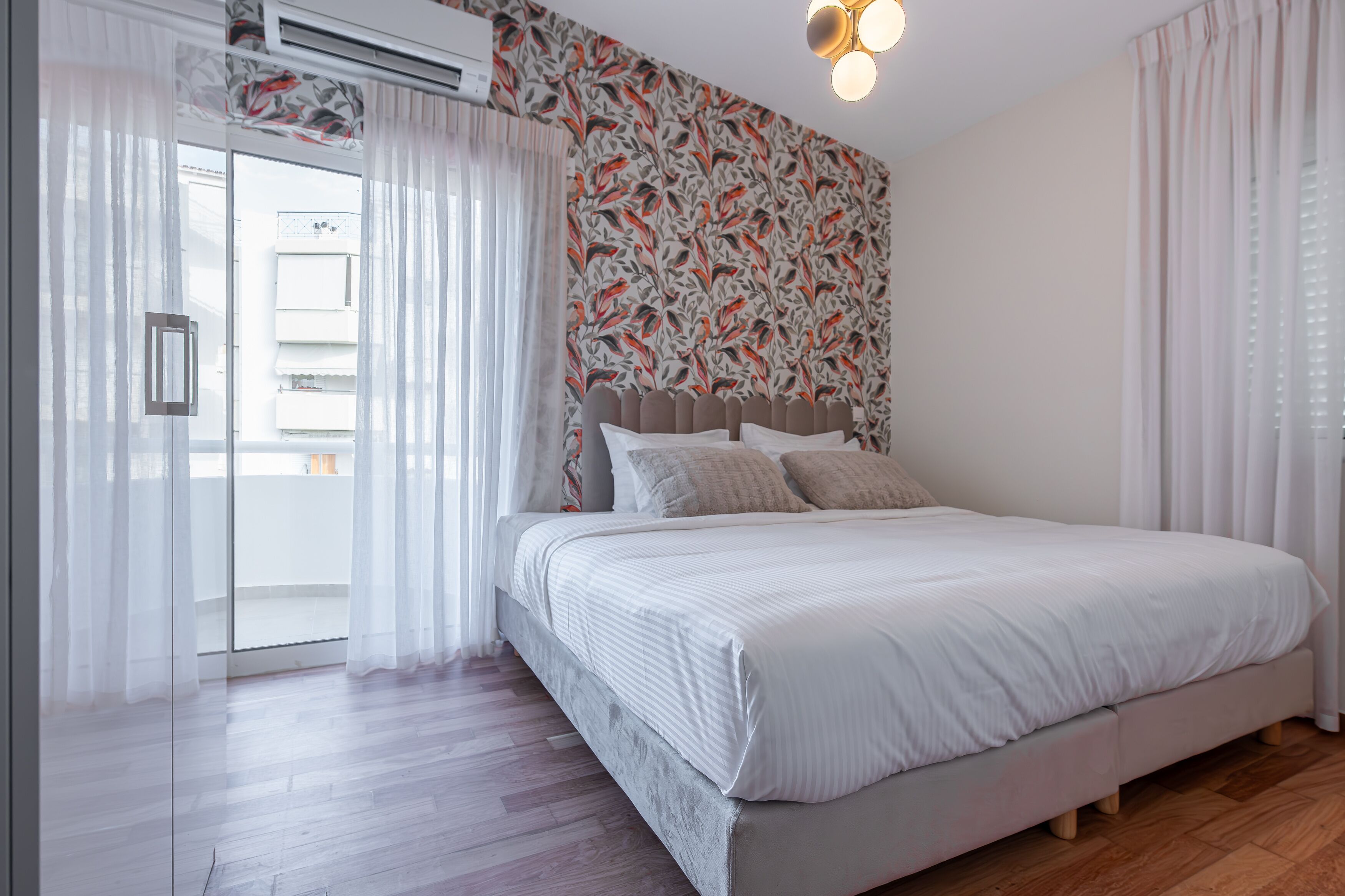 A bedroom with a bed, a window with curtains, a patterned wall, and an air conditioning unit.