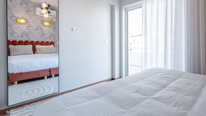 Ein Schlafzimmer mit einem Bett, einem großen Spiegel und einem Fenster mit durchsichtigen Vorhängen.