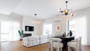 Ein modernes Wohnzimmer mit einer Couch, einem Esstisch, Stühlen und einem an der Wand befestigten Fernseher.