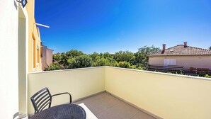 A balcony with a table and chairs, a clear blue sky, and a view of neighboring buildings and greenery. - Apartment with pool in Medulin A6 (Medulin)