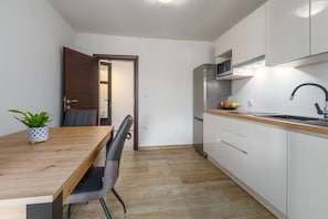 A compact kitchen with white cabinets, a wooden countertop, a stainless steel refrigerator, and a microwave.