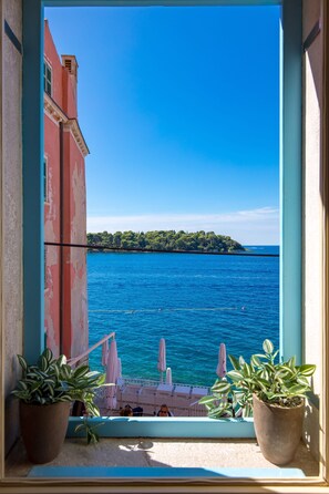 A balcony with potted plants, a view of the sea, and a distant island.