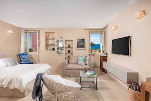 A bedroom with a bed, a sofa, a chair, a TV, and a view of the sea. - Natascha’s Beachfront / Boutique Studio Apartment A1 (Rovinj)