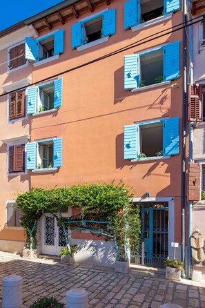 Un edificio con varias ventanas, algunas con contraventanas, y una puerta con reja de metal.