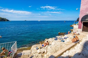 A coastal scene with rocky terrain, a clear blue sky, and a calm sea. - Natascha’s Beachfront / Boutique Studio Apartment A1 (Rovinj)