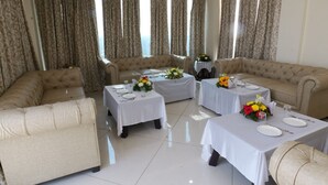 A spacious living area with three beige sofas, two round tables with white tablecloths, and floral centerpieces.