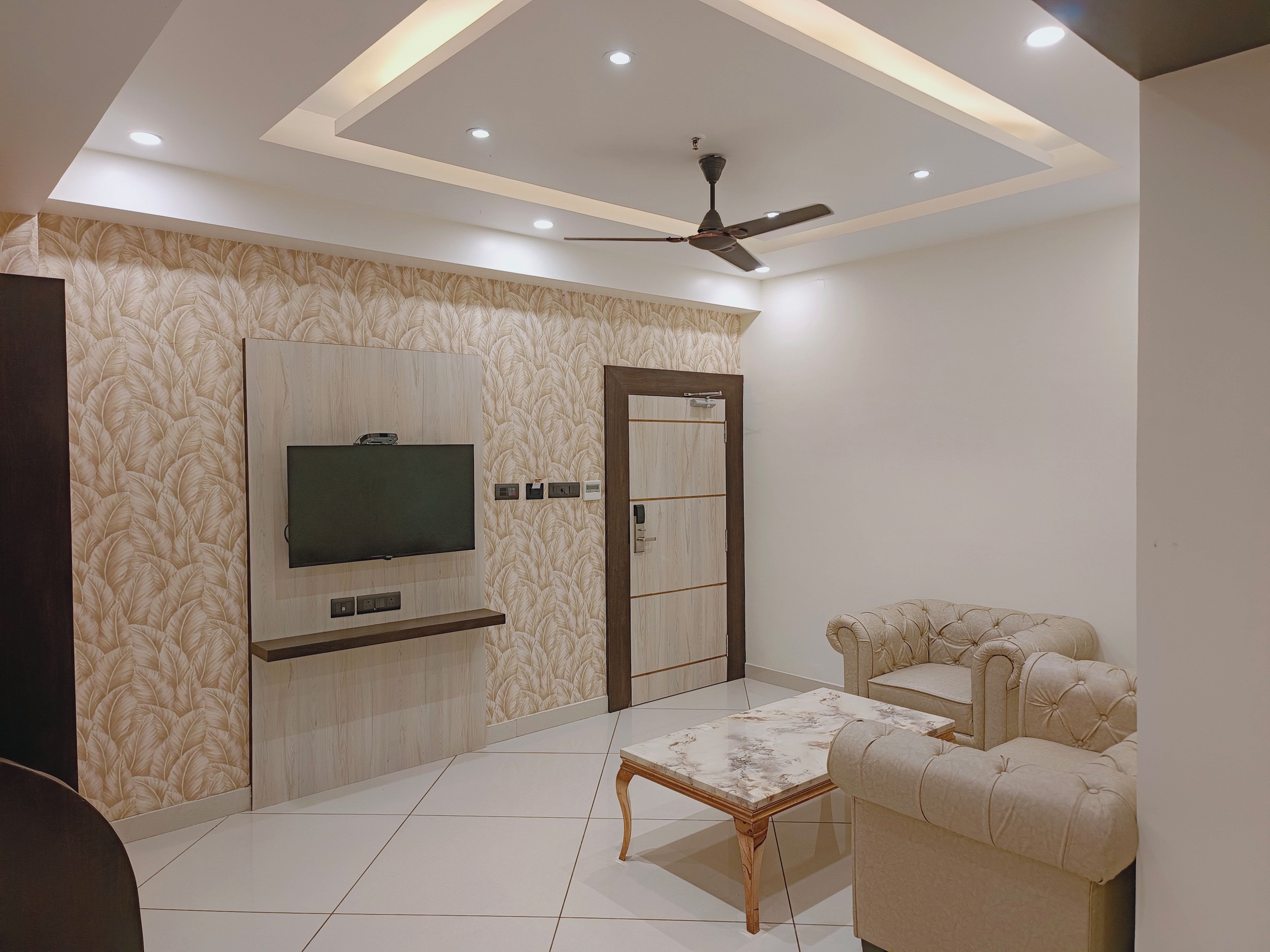 A modern living room with a flat-screen TV, a ceiling fan, and a tufted sofa.