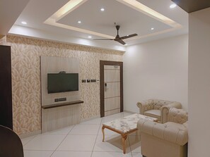 A modern living room with a flat-screen TV, a ceiling fan, and a tufted sofa. - 7 Hills Hotel & Resort (Rajgir)