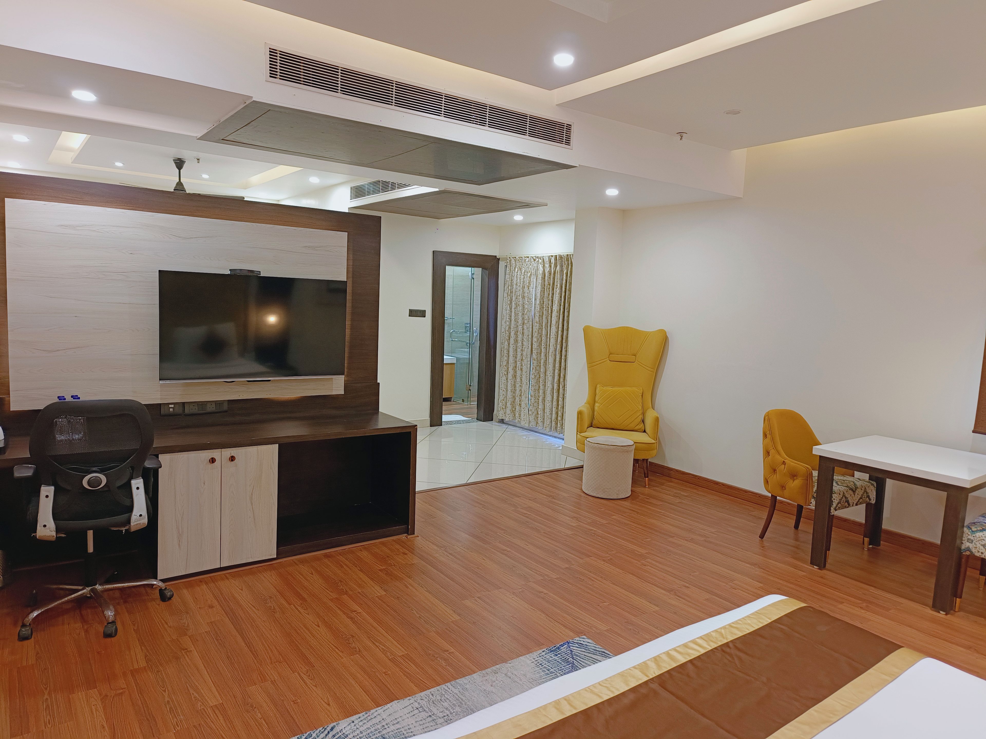 A modern living room with a flat-screen TV, wooden flooring, a yellow armchair, a small round table, and a sofa.