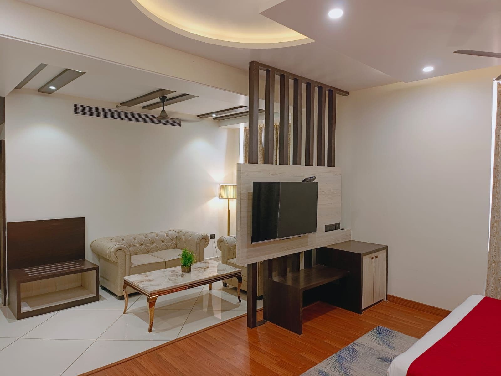 A modern living room with a sofa, a coffee table, a TV mounted on a wooden wall, and a ceiling fan.