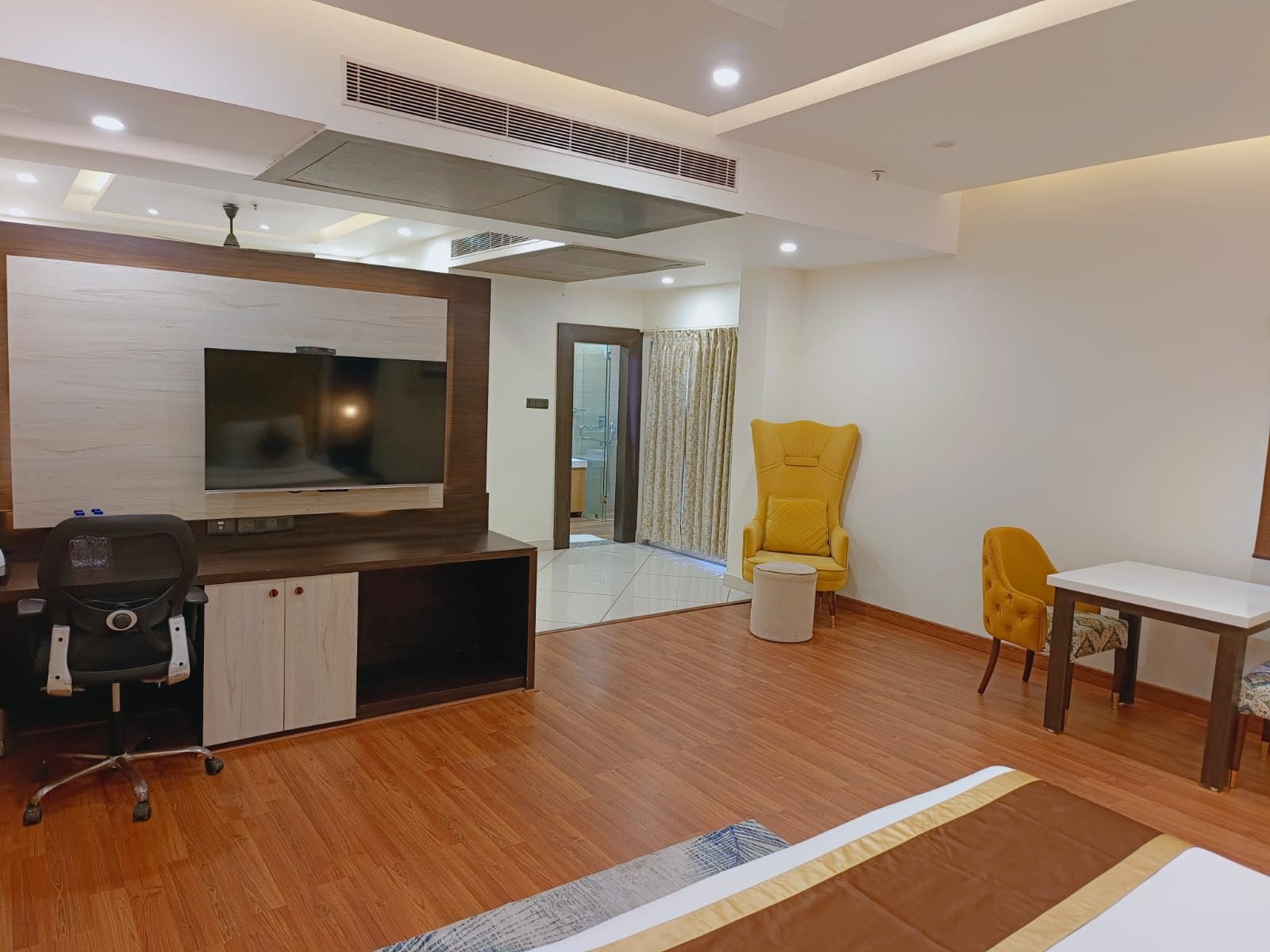 A modern living room with a flat-screen TV, wooden flooring, a yellow armchair, a small round table, and a sofa.