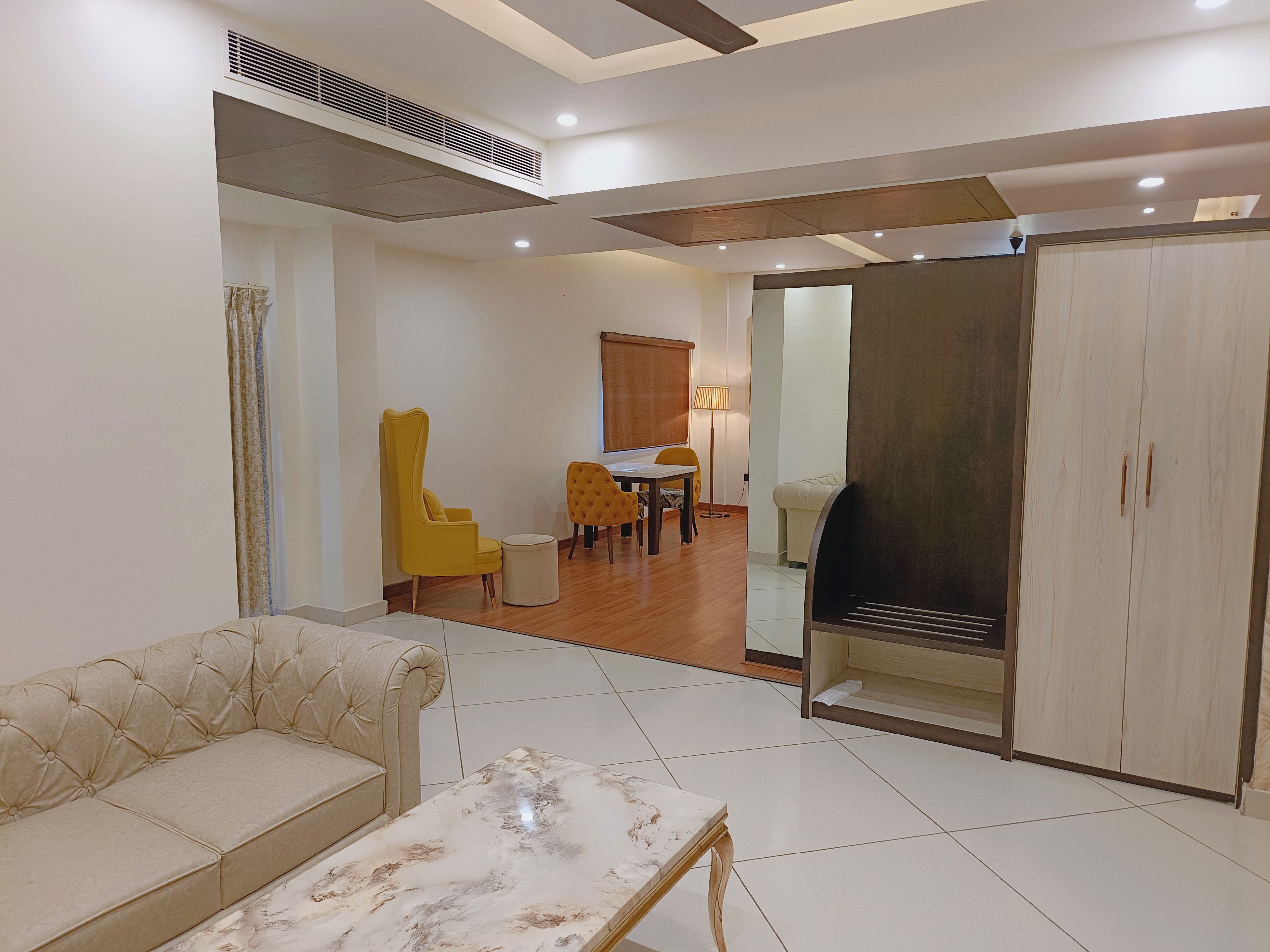 A living room with a sofa, a coffee table, a dining area with chairs, and a wardrobe.