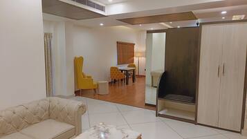 A living room with a sofa, a coffee table, a dining area with chairs, and a wardrobe.