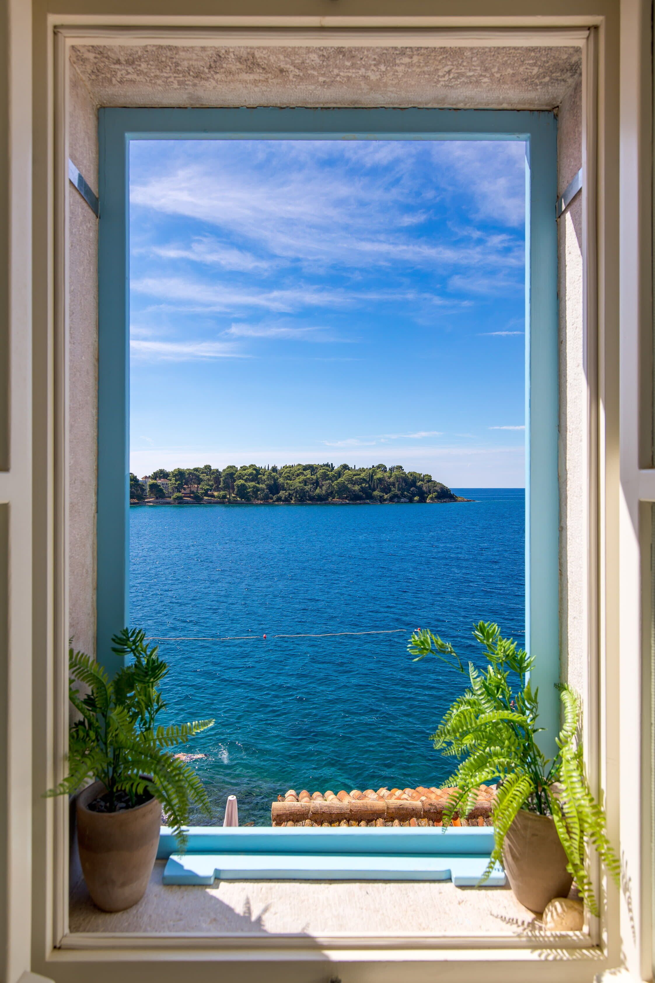A window with a view of a calm sea and a distant island.