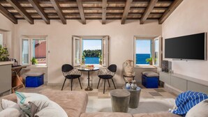A living room with a wooden ceiling, a TV mounted on the wall, a dining table with chairs, and a view of the sea through large windows. - Natascha’s Beachfront/Stylish Two-Story Apartment A2 (Rovinj)