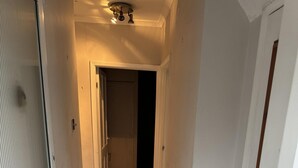 Un couloir étroit aux murs blancs, doté d’un sol carrelé et d’un luminaire au plafond.