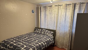 Une chambre à coucher avec un lit, des rideaux, un luminaire au plafond et une horloge murale.