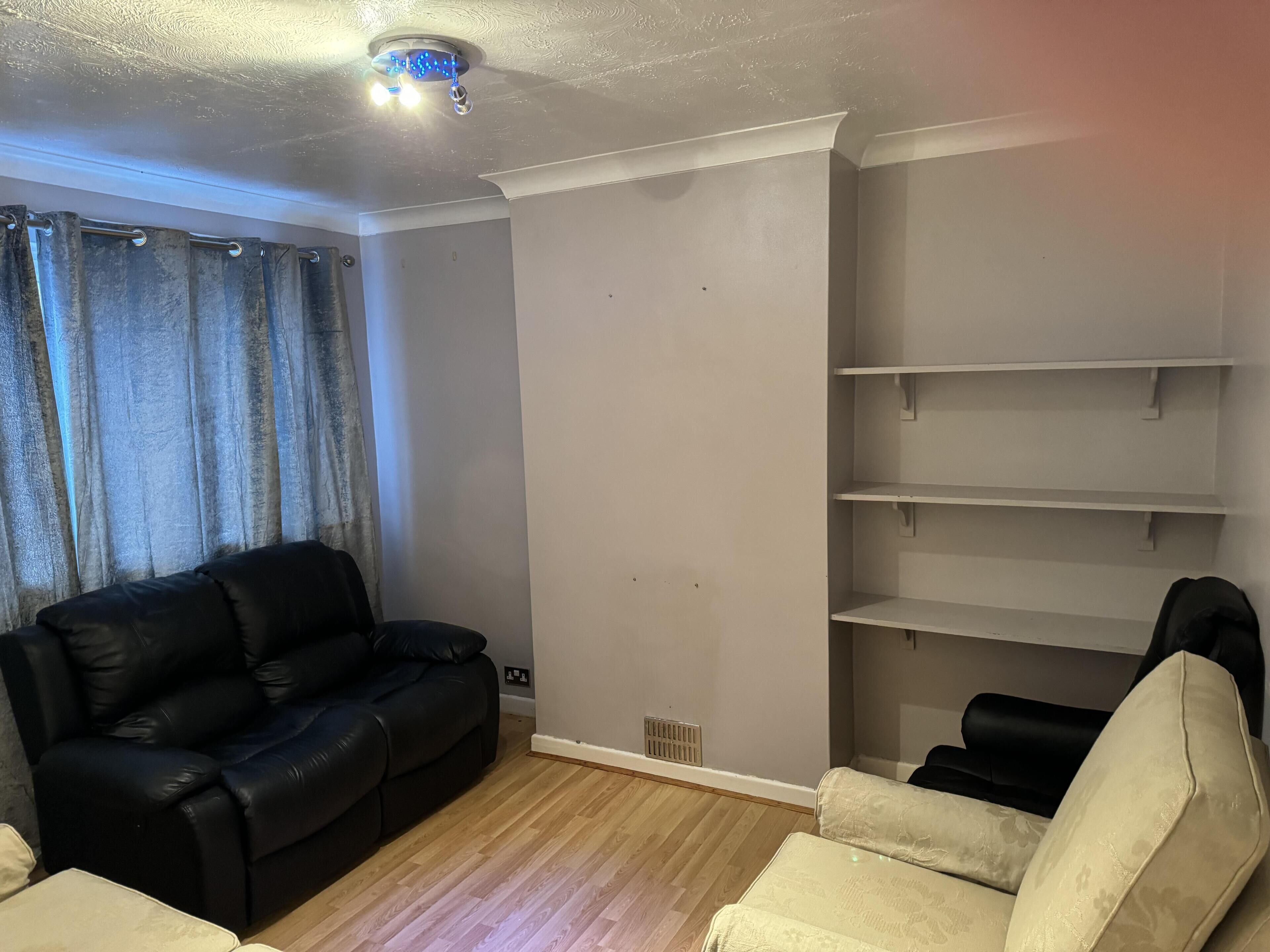 Een woonkamer met een zwarte leren bank, een beige fauteuil en een witte wandplank.