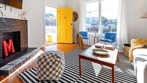 A living room with a fireplace, a checkered ottoman, a coffee table, and a view of the outside through large windows. - Suite Tea (Atlanta)