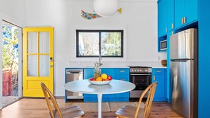 A modern kitchen with blue cabinets, a stainless steel refrigerator, and a round white table with two wooden chairs. - Suite Tea (Atlanta)