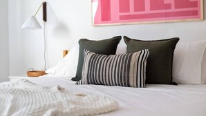 A neatly made bed with two pillows, a bedside lamp, and a framed artwork on the wall. - Suite Tea (Atlanta)