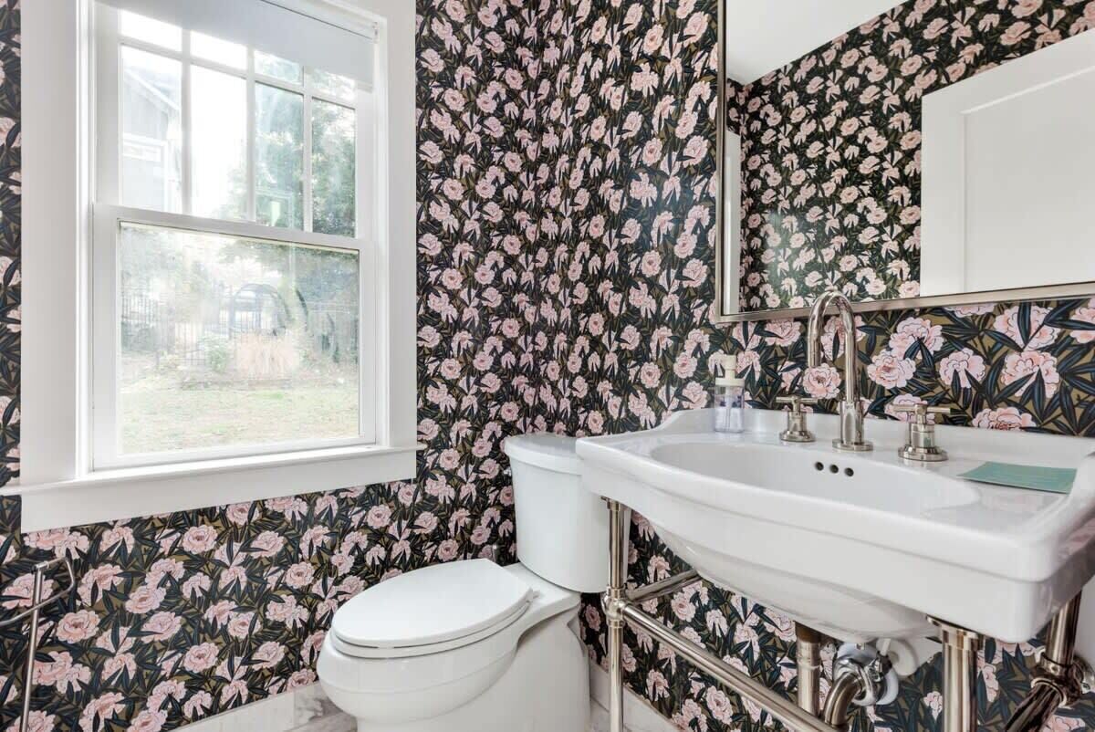 Un baño con papel tapiz floral, un inodoro blanco y un lavabo con espejo.