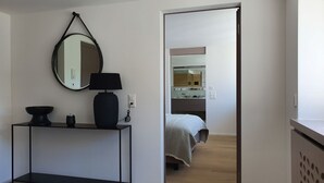 Un dormitorio moderno con cama, mesita de noche, espejo y consola con lámpara.