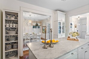 A modern kitchen with white cabinetry, a marble countertop, and a dining area with a white table and chairs. - "The Broadway Hideaway" by Roxy Rentals (Wayzata)