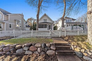 A residential area with a white picket fence, stone steps leading to a house, and a clear sky. - "The Broadway Hideaway" by Roxy Rentals (Wayzata)