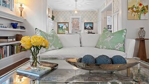 Un salón moderno con un sofá blanco, cojines decorativos, una mesa de centro de cristal y un jarrón con rosas amarillas.