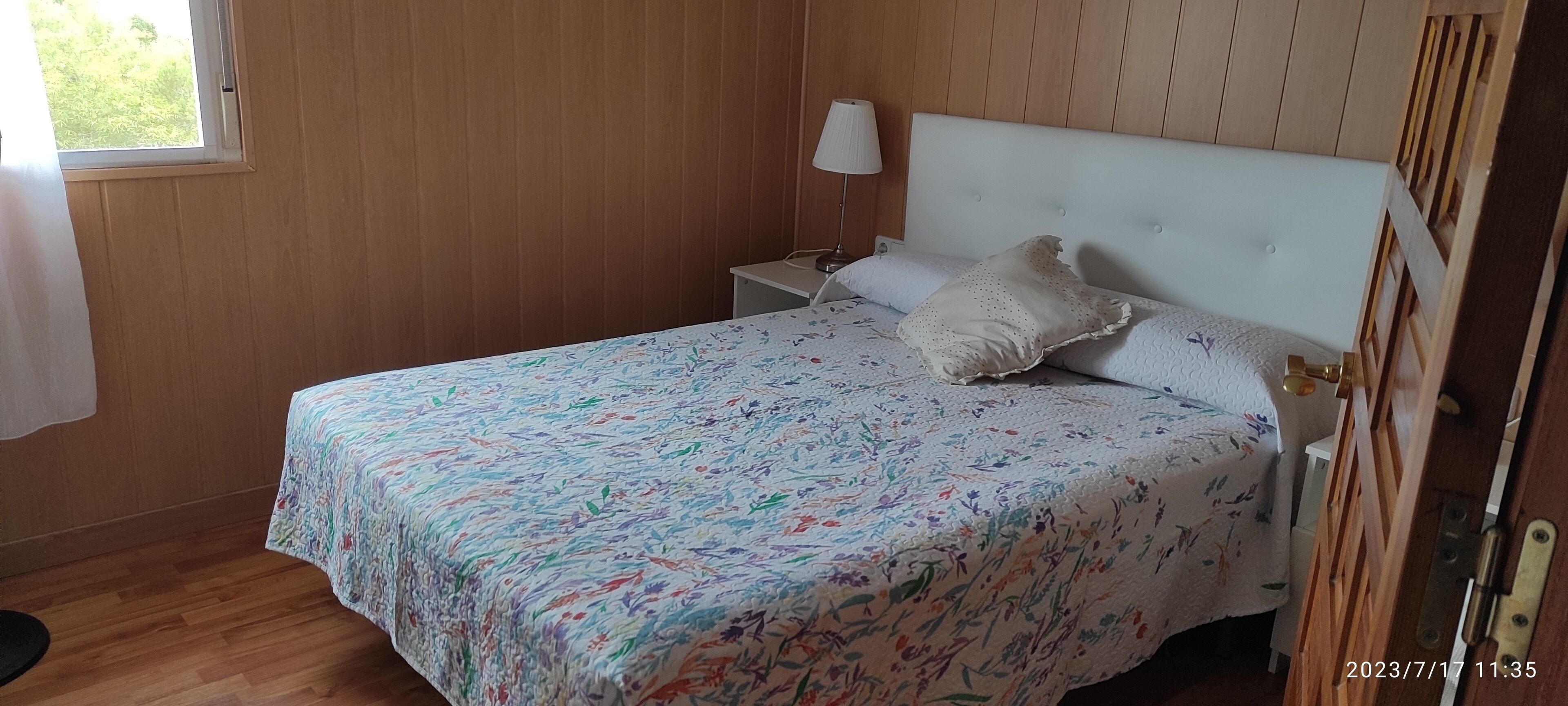 Une chambre à coucher avec un lit, une table de chevet, une lampe et une fenêtre.