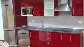 Een keuken met rode kastjes, een roestvrijstalen koelkast, een magnetron en een spoelbak.