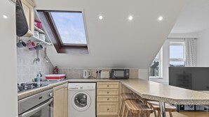 A compact kitchen with a washing machine, microwave, and wooden stools. - Cosy Flat In London (London)