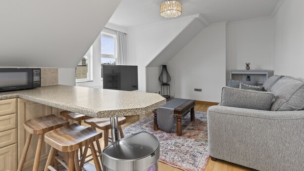 A modern kitchen with a large island, wooden stools, a built-in microwave, and a pendant light. - Cosy Flat In London  (London)